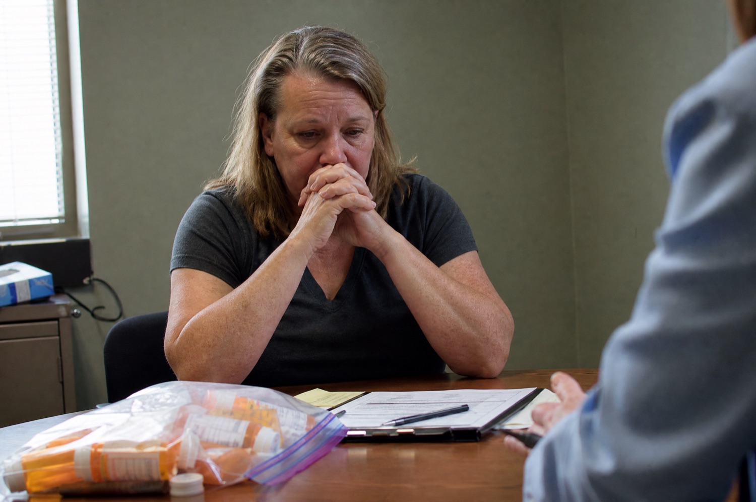 A woman in her fifties sitting across from a clinician with a bag of prescription bottles on the table