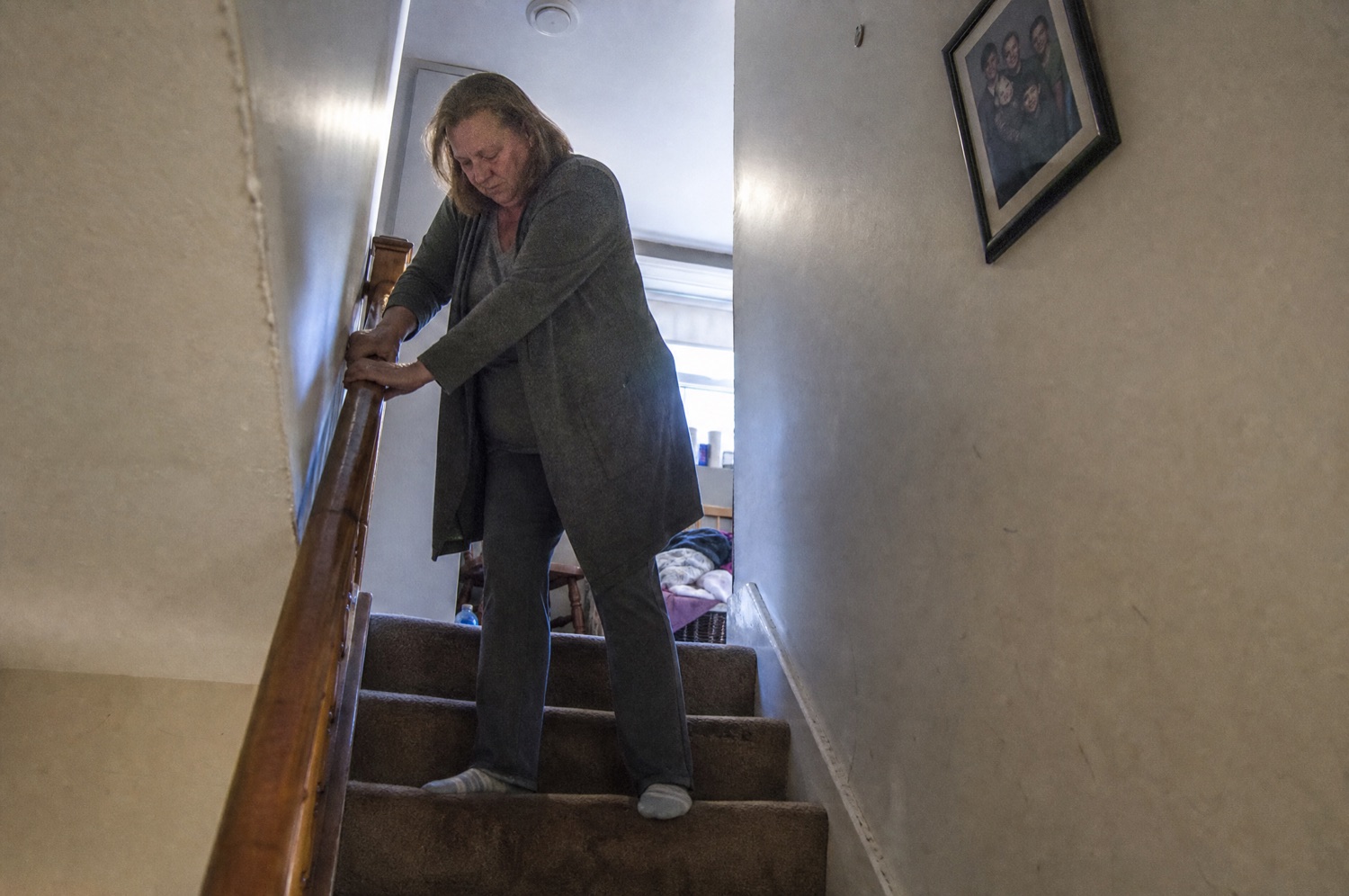 A woman stopped partway up a staircase gripping the banister